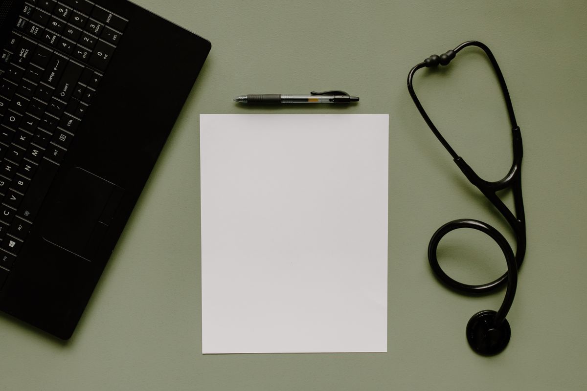 A stethoscope, pen and blank page on a desk beside a laptop